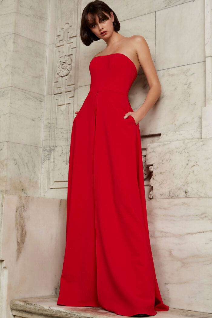Model wearing Jovani 03529 red jumpsuit, front view with elegant pose, showcasing unique wide-leg overlay.