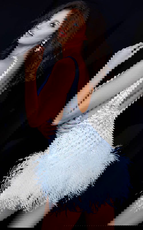 Model showing back of Jovani 05535 white dress featuring feather hem and sequins.