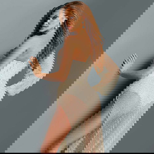 Back view of model wearing Jovani 06082 nude gown with sheer sleeve and high slit.