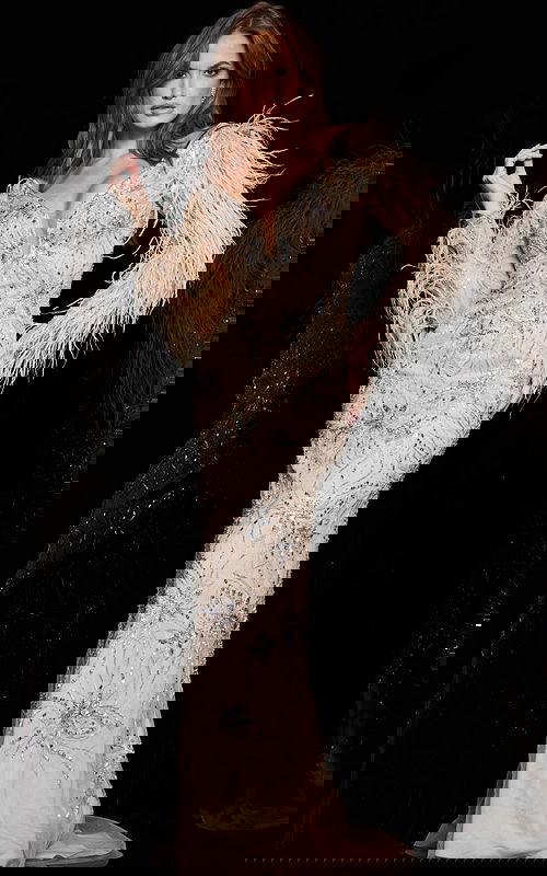 Model wearing Jovani 06305 nude gown with feather details and embellishments, angled front view.