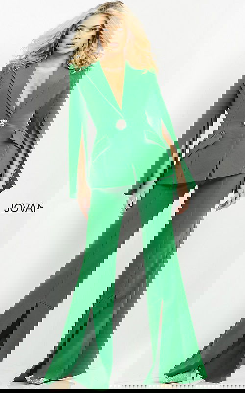 Model wearing Jovani 06922 emerald green jumpsuit with cape sleeves and brooch detail, front view.