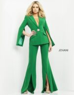 Model wearing Jovani 06922 emerald green jumpsuit with cape sleeves and brooch detail, front view.