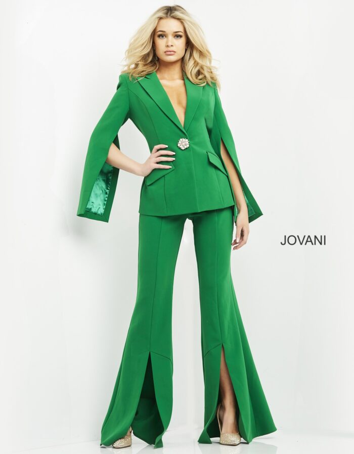 Model wearing Jovani 06922 emerald green jumpsuit with cape sleeves and brooch detail, front view.