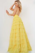 Model wearing Jovani 08480 yellow gown with open back, cascading ruffles.