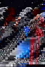 Model wearing Jovani 79121 black gown with another person in a red suit.