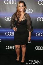 Model wearing Jovani 88586 black dress with sheer gold-detailed cape sleeves