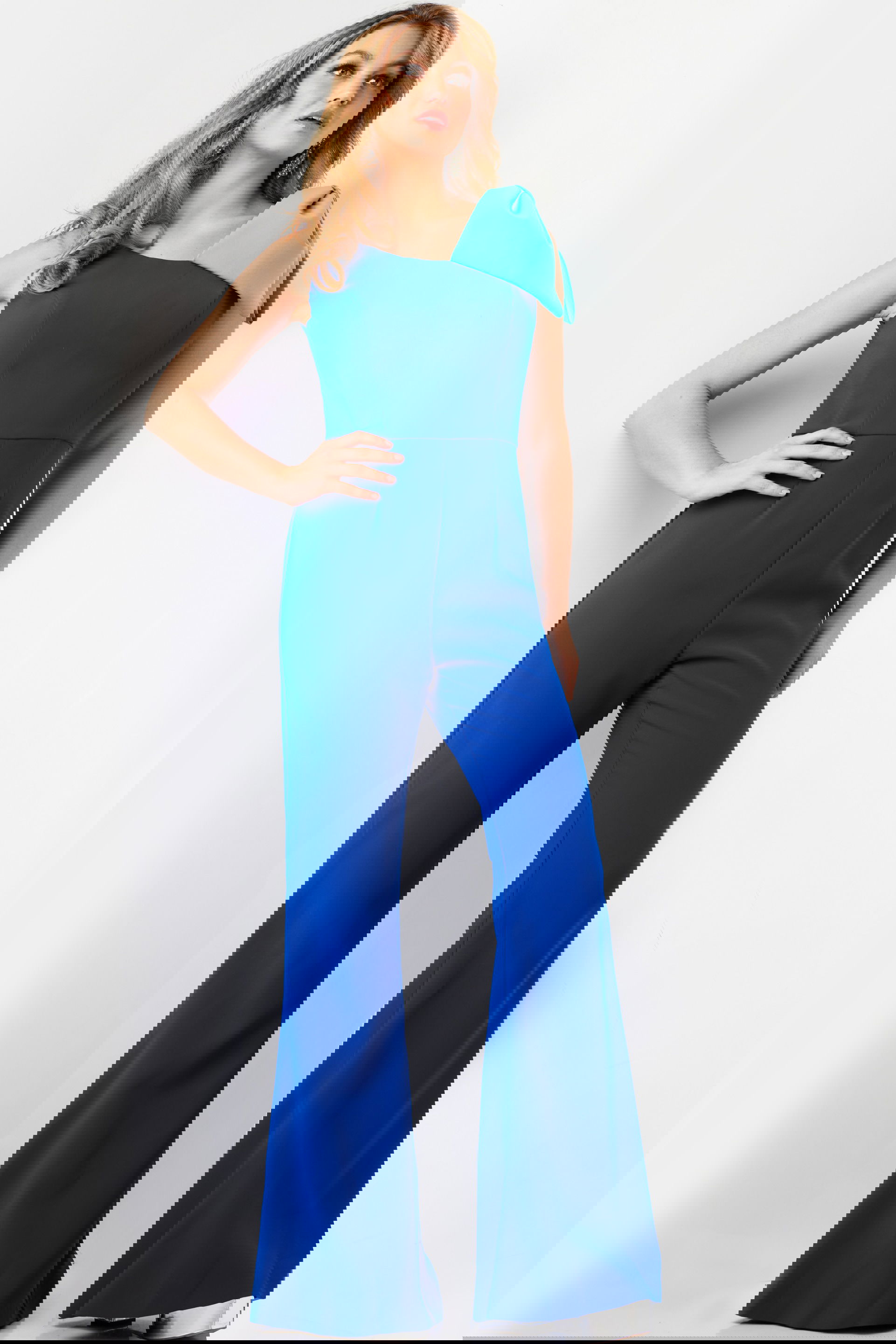 22589-ROYALTURQ-15.jpg Model wearing Jovani 22589 royal blue jumpsuit with one-shoulder and bow detail, front view.