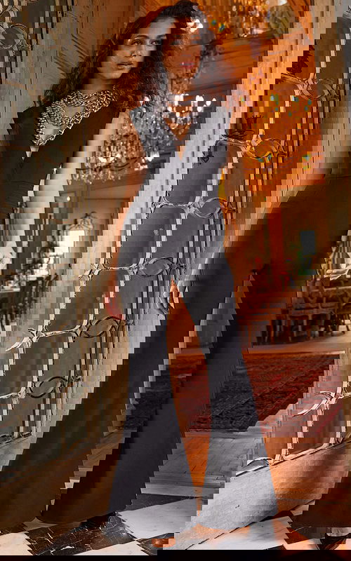 Model wearing Jovani 23240 black jumpsuit with deep V-neck and layered chains.