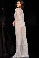 Back view of model wearing Jovani 23895 nude dress showing cape details.