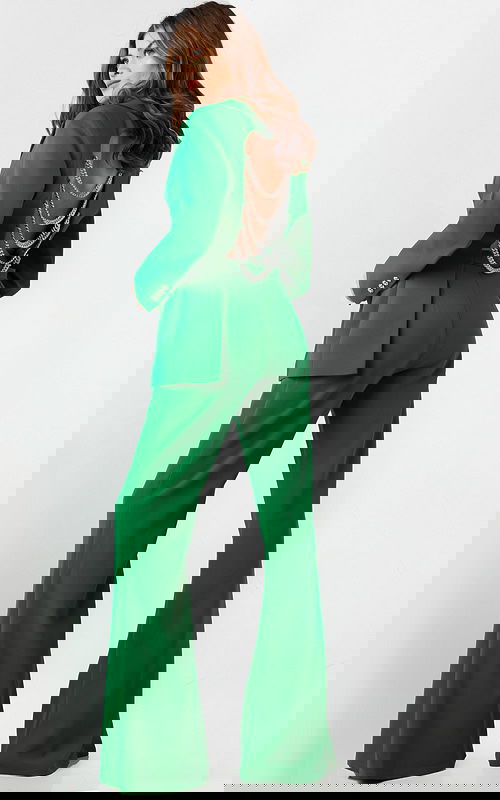 Model wearing Jovani 26144 green pantsuit with open back and chain detailing.