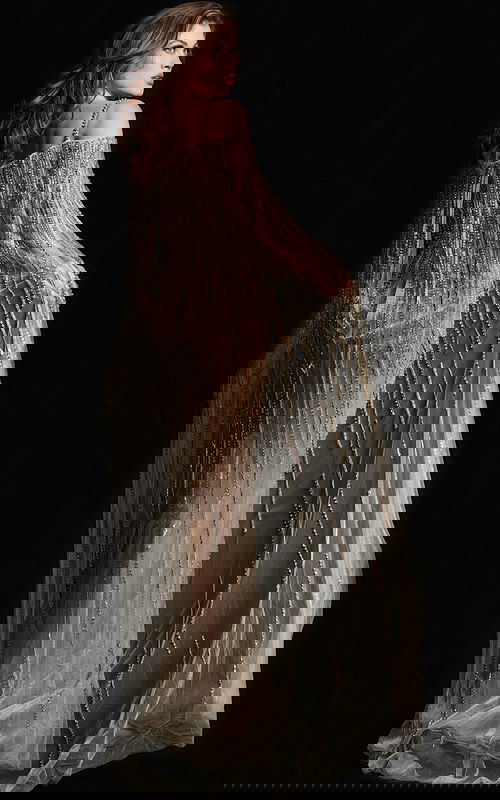 Back view of model in Jovani 26324 gold gown showing intricate beadwork and cape.