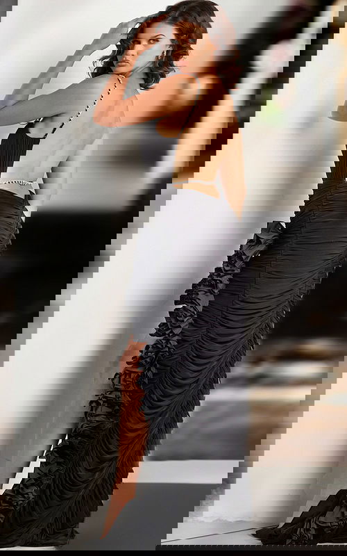 Model wearing Jovani 34392 black gown showing open back design and ruffled slit.