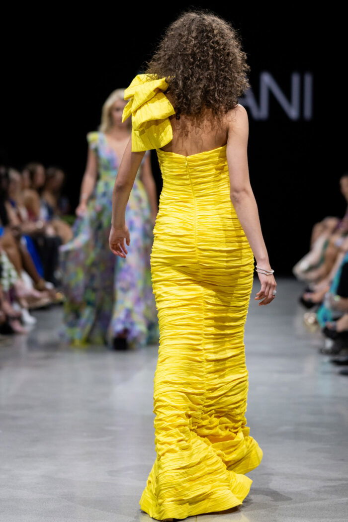 Model showcasing the back view of Jovani 38240 dress in yellow with detailed ruching.