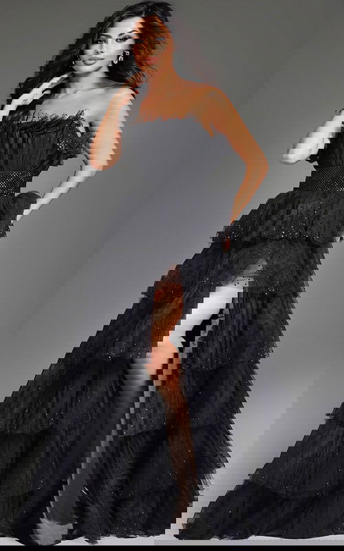 Model wearing Jovani 38301 black strapless gown with tiered layers and high slit.