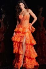 Model wearing Jovani 38528 orange gown with floral embroidery and tiered ruffles from the front