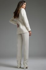 Model wearing Jovani 39726 ivory pant suit with silver embellishments, back view.