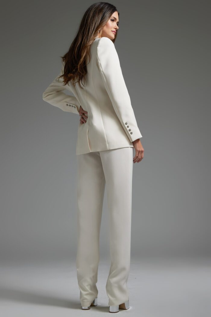 Model wearing Jovani 39726 ivory pant suit with silver embellishments, back view.