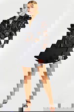 Woman wearing sheer black lace blouse with layered ruffle collar and flared black mini skirt