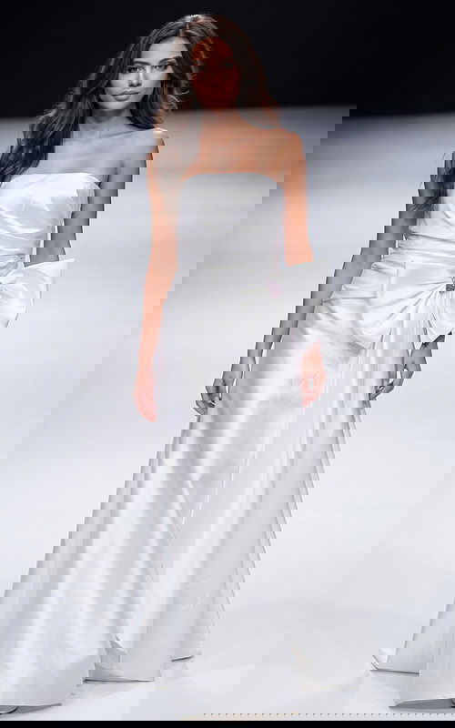 Strapless floor length gown with a smooth fitted bodice, soft draping, and an oversized bow detail at the waist creating a clean, elegant silhouette