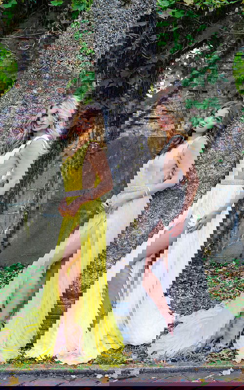 Two models showcasing Jovani S63599 yellow and white gowns with V-necklines and slits.