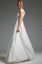 Model wearing Jovani JB05402 shows side view of off-the-shoulder white dress.