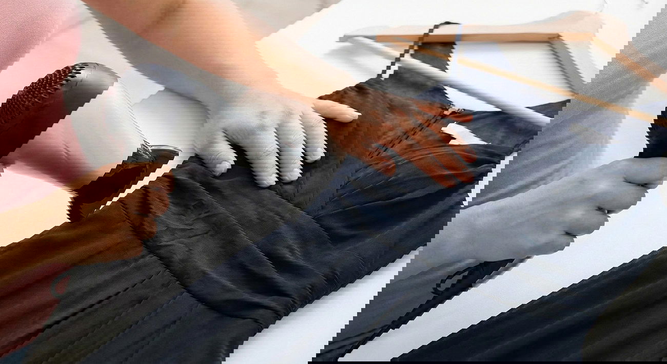 Someone using a hair dryer to remove wrinkles from a dress