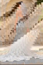 Back view of a strapless lace mermaid gown with sheer back, button closure, and long tulle train.