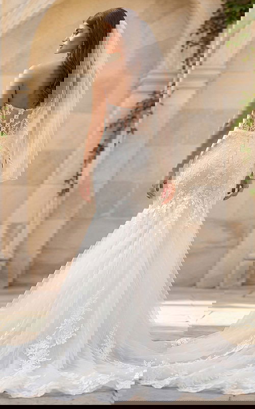 Back view of a strapless lace mermaid gown with sheer back, button closure, and long tulle train.