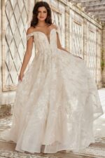 Model in front of JB220001 ivory gown with lace and off-the-shoulder sleeves.