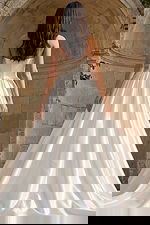 Back view of a strapless satin bridal gown with pleated ball skirt and chapel train set against stone arches