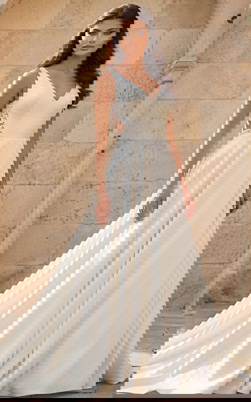 Front view of an elegant V-neck bridal gown with smooth skirt and lace side panels in an outdoor stone courtyard.