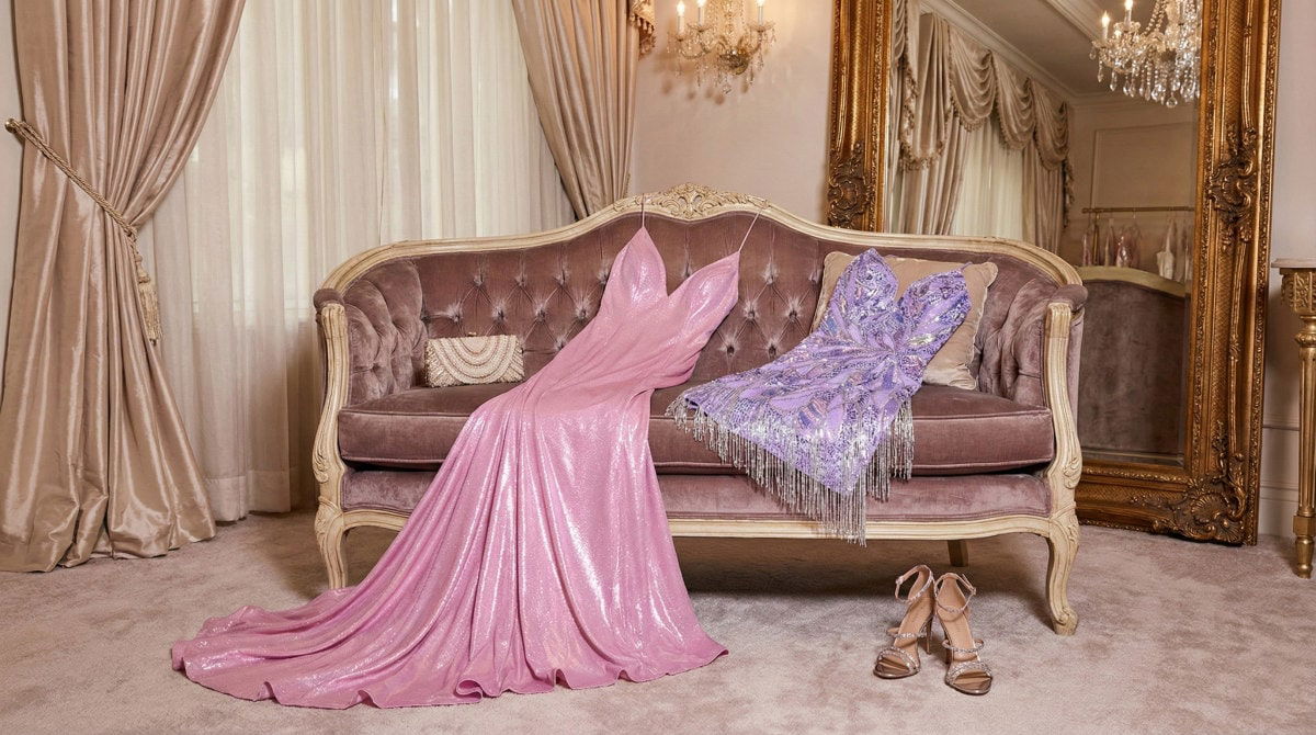 Comparison of a long pink sequin prom dress and a short purple fringed homecoming dress displayed on a velvet sofa.