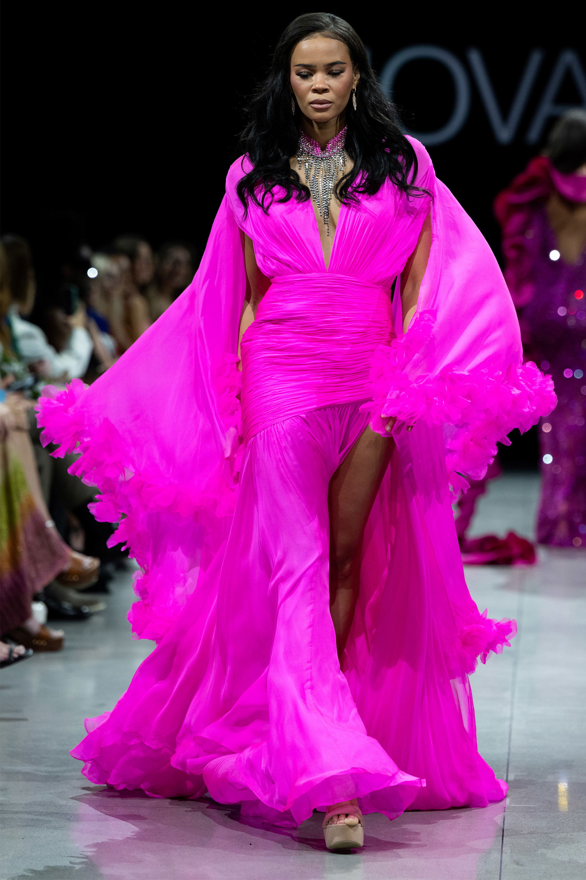 S36352.jpg model wearing S36352 vibrant pink gown with plunging neckline and cape sleeves