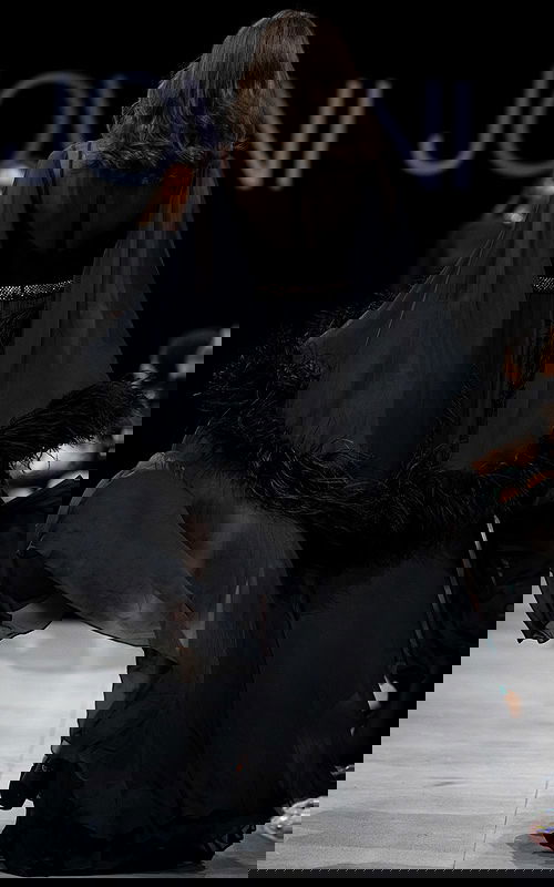 Model wearing S39276 black gown, back view with sheer feathered sleeves.