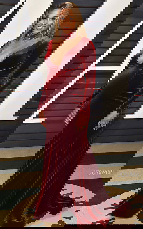 Model wearing Jovani S55169 burgundy velvet gown with deep V-neckline and long sleeves.